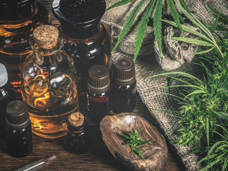 CBD oil bottles and green plant of cannabis on a wooden background. Herbal medicine.