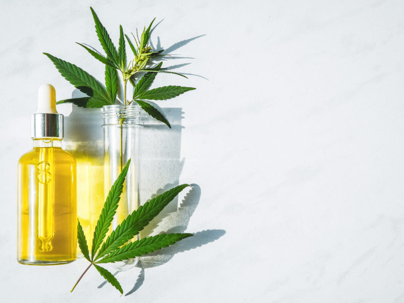 Glass bottle with cannabis oil and a test tube with hemp leaves on a marble background. Copy space flat lay, top view, trending,